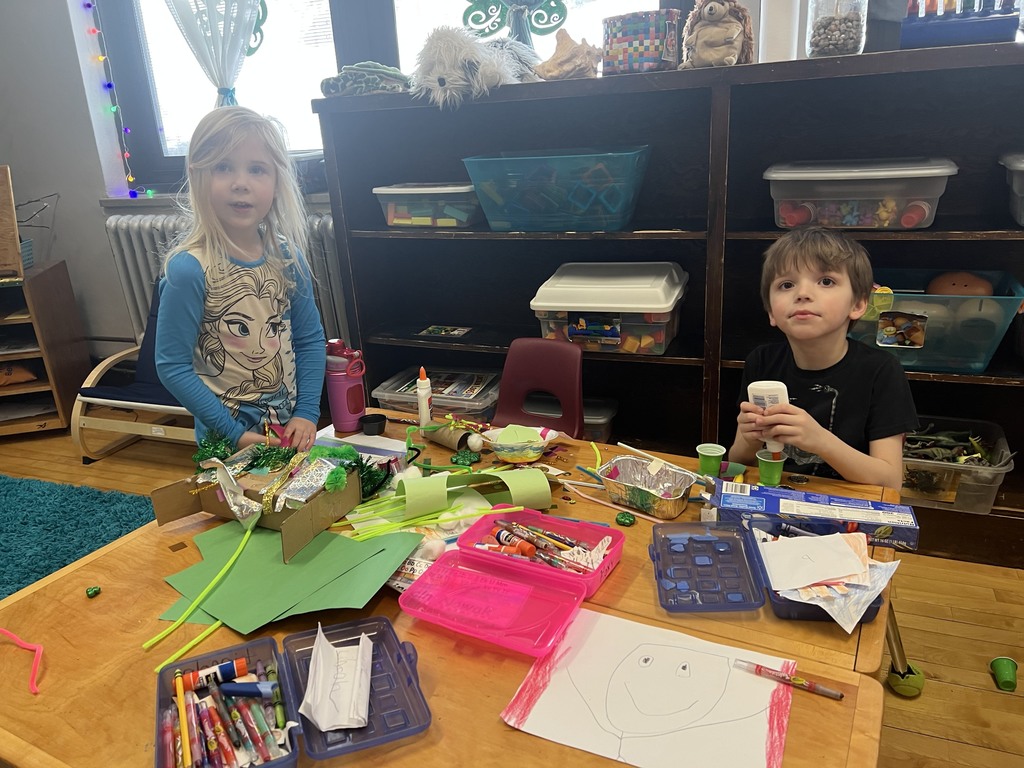 One student puts glue in a cup while the other works on the box