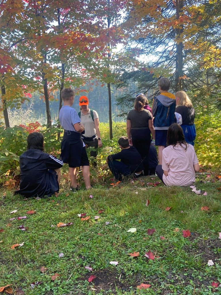 Students sit and listen to a camp counselor in the woods