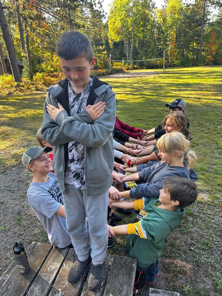 A student stands at the edge of a picnic table, ready for a trust fall